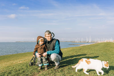 People with cat at riverbank against sky