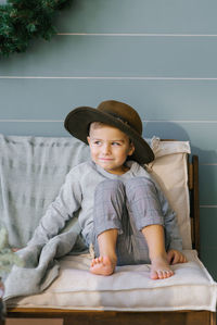 Prankster a happy child boy is sitting on the sofa in a hat that he took from his mother person
