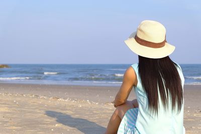 Woman wearing hat while sitting at beach against sky