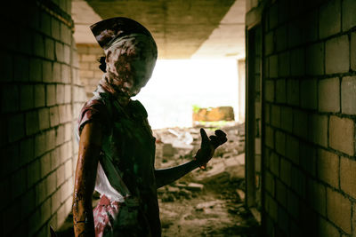 Spooky woman in mask standing at abandoned building corridor