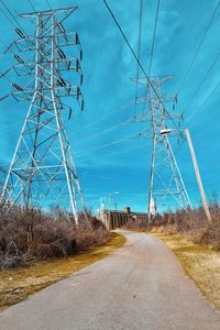 Road by electricity pylon against sky
