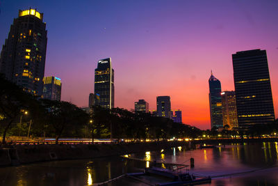 Illuminated buildings by river against sky in city at night