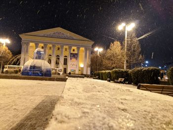 Illuminated street by building during winter at night