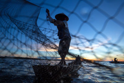 Man fishing with net by sea against sky