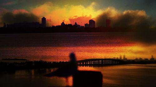 Silhouette of city at waterfront during sunset