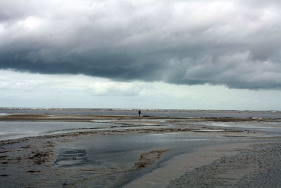 View of calm beach against cloudy sky