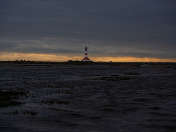 Lighthouse by sea against sky during sunset