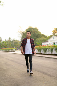 Portrait of young man standing on road against sky