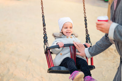 Cheerful cute girl sitting on swing at playground