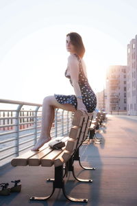 Young woman on seat in city against sky