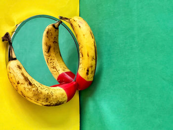 Red tipped bananas on mirror on yellow and green background.