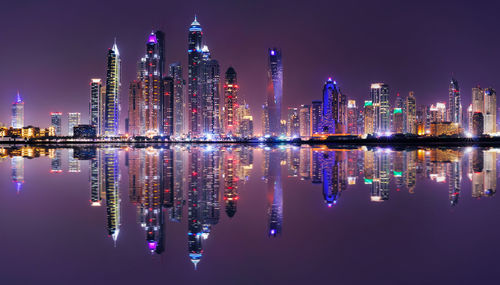 Reflection of illuminated buildings in river against sky at night