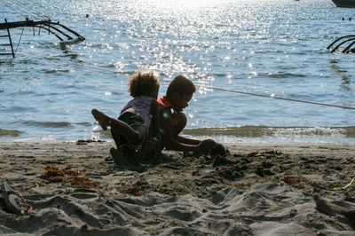 Rear view of boys sitting on beach