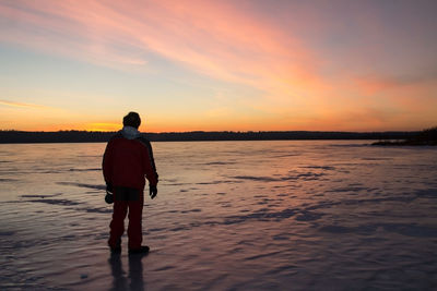 Rear view of man standing on beach during sunset