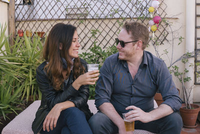 Smiling couple holding beer while sitting outdoors