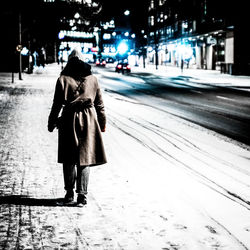 Rear view of woman walking on snow covered road