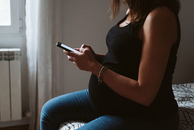 Midsection of pregnant woman using phone while resting at home