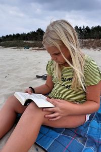 Girl with blond hair reading book sitting at beach