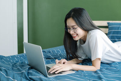 Young woman using mobile phone while sitting on bed