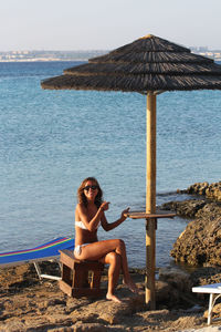 Portrait of woman wearing bikini while sitting on rocky shore