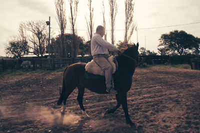 Side view of man riding horse in a rural area