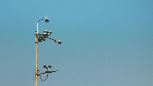 Low angle view of street light and security cameras against clear blue sky