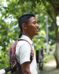 Profile view of young man smiling while standing against trees