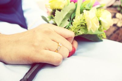 Close-up of hand holding flower bouquet, with engagement ring on finger.