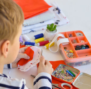 A caucasian boy of 9 years old is learning to sew with his hands a homemade gift for mom