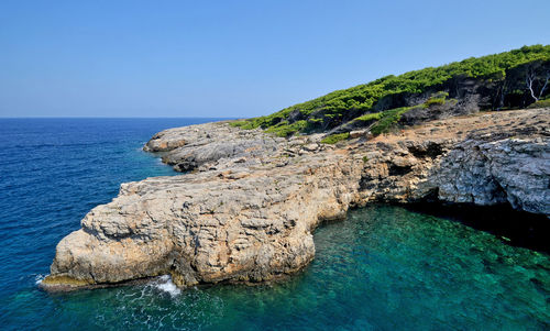 Rock formations by sea against clear blue sky