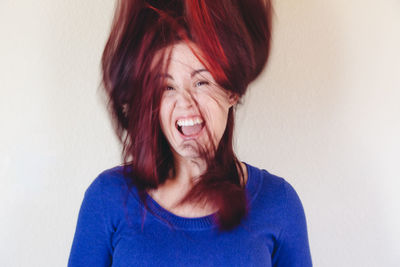 Portrait of laughing young woman with tousled hair against wall