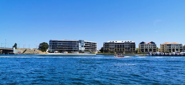 Sea by buildings against clear blue sky