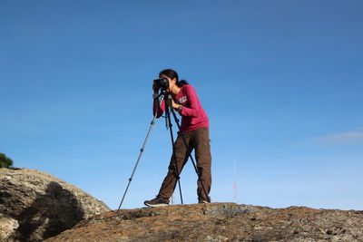 Man photographing on rock against sky