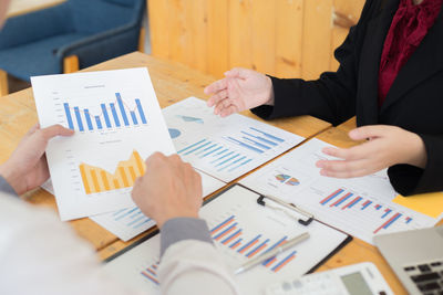 Cropped image of business colleagues analyzing graph on desk in office