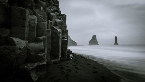 Reynisdrangar rock formation at beach against cloudy sky