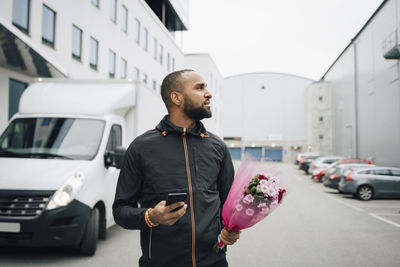 Male worker with bouquet of flower and smart phone searching in city