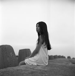 Sad woman sitting on retaining wall against sky