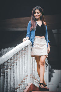 Portrait of a smiling young woman standing against railing