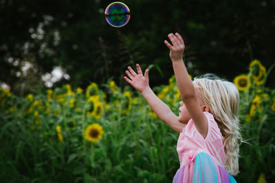 Side view of girl with arms raised looking at bubble flying in mid-air