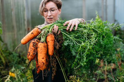 Smiling woman holding carrots at farm