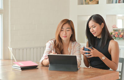 Young woman using phone while sitting on table