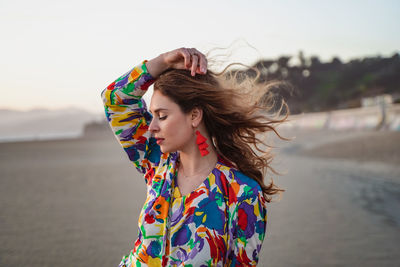 Young woman standing at beach against sky
