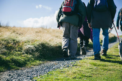 Low section of hikers with dog walking on trail against sky