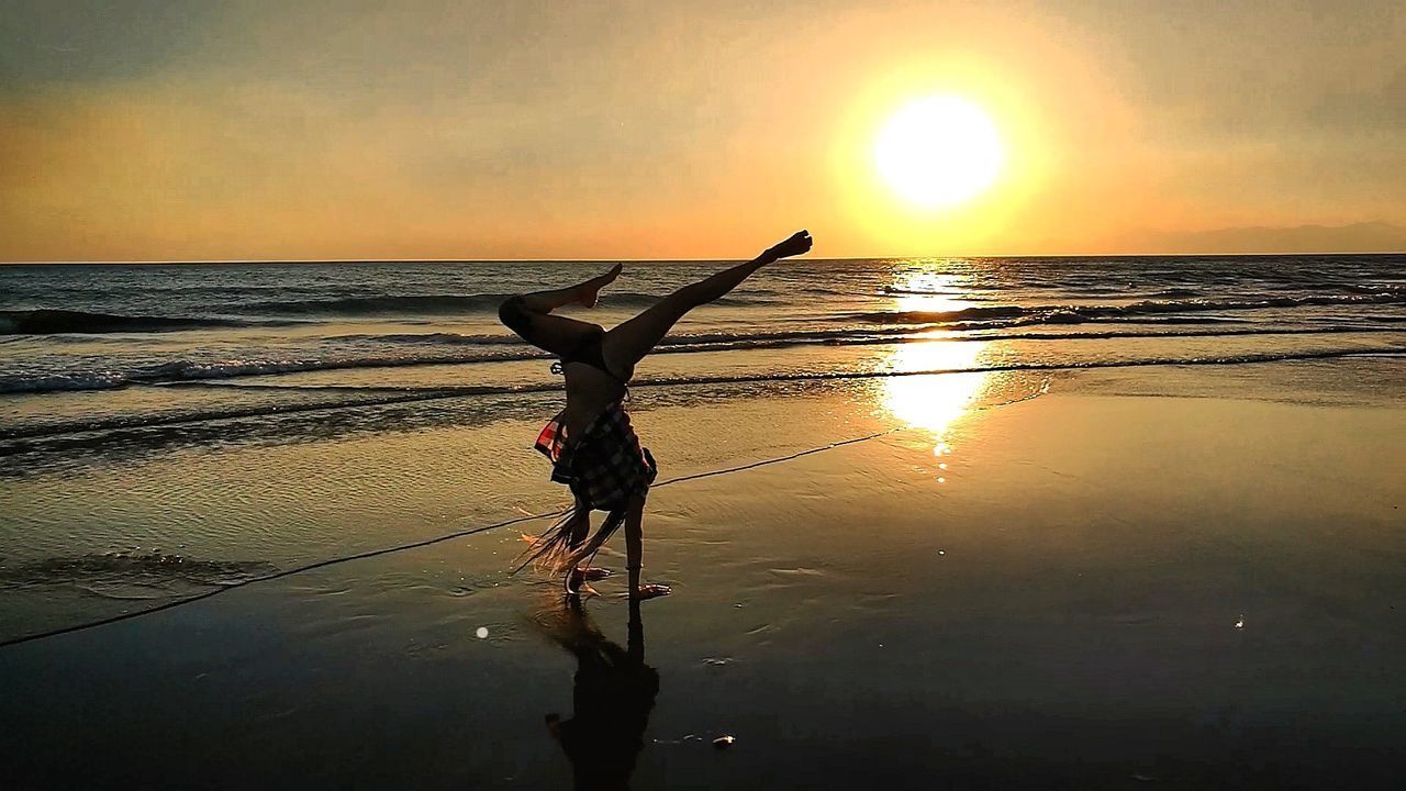 SILHOUETTE WOMAN ON BEACH AGAINST ORANGE SKY