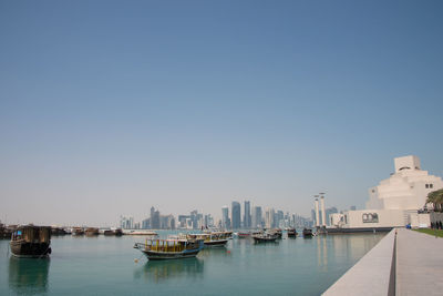 Sailboats moored on sea by buildings against clear sky