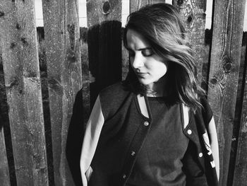 Young woman with eyes closed standing by wooden fence during sunny day