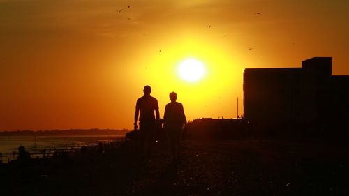 Silhouette men on shore against sky during sunset
