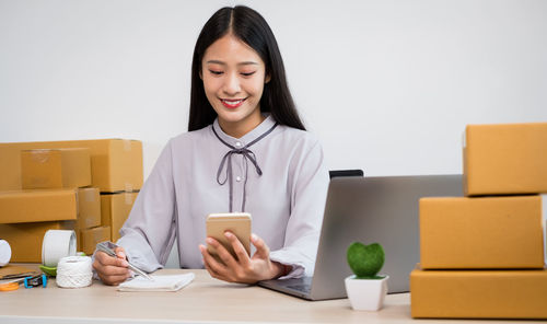 Smiling young woman using smart phone while sitting in office