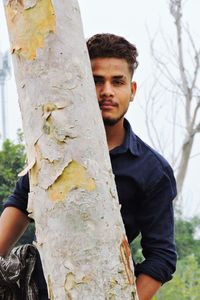 Full length of young man standing by tree trunk