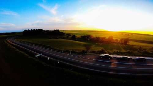 Panoramic shot of road amidst field against sky during sunset